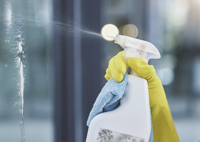 Professional cleaner spraying and wiping a window as part of residential and commercial cleaning services in Phoenix.